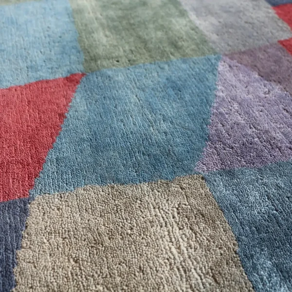Närbild. Handgjord matta tillverkad av Rug Your Life, inspirerad av Paul Klees målning ”Eld i fullmåne”. Mattan har färgerna mörkblått, rött, lila, mörkgrönt och en touch av gult.