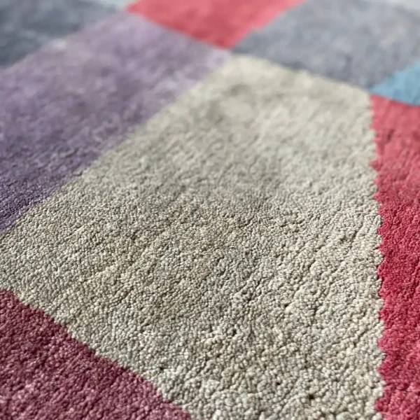 Närbild. Handgjord matta tillverkad av Rug Your Life, inspirerad av Paul Klees målning ”Eld i fullmåne”. Mattan har färgerna mörkblått, rött, lila, mörkgrönt och en touch av gult.