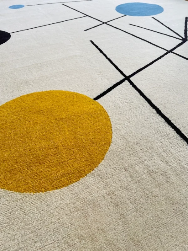 Gros plan du tapis artisanal sur mesure inspiré du tableau « Équilibre » de Sophie Taeuber-Arp. Les couleurs principales du tapis sont le blanc, le jaune, le bleu et le noir. Tapis en édition limitée numérotée, par Rug Your Life.