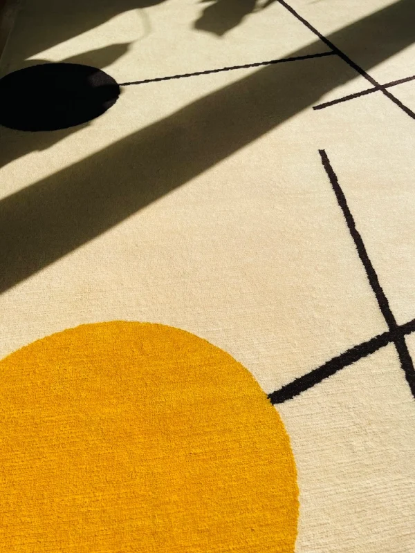 Gros plan du tapis artisanal sur mesure inspiré du tableau « Équilibre » de Sophie Taeuber-Arp. Les couleurs principales du tapis sont le blanc, le jaune, le bleu et le noir. Tapis en édition limitée numérotée, par Rug Your Life.