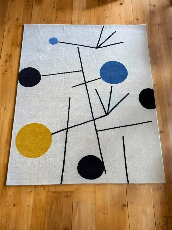 Tapis artisanal sur mesure inspiré du tableau « Équilibre » de Sophie Taeuber-Arp. Les couleurs principales du tapis sont le blanc, le jaune, le bleu et le noir. Tapis en édition limitée numérotée, par Rug Your Life.