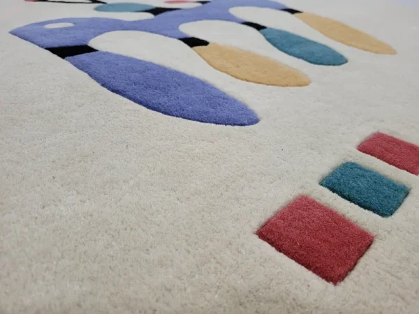 Gros plan sur tapis fait main par Rug Your Life, inspiré du tableau « Composition » (1944) de Wassily Kandinsky. Les couleurs du tapis sont le blanc crème, le bleu, le rouge et le vert.