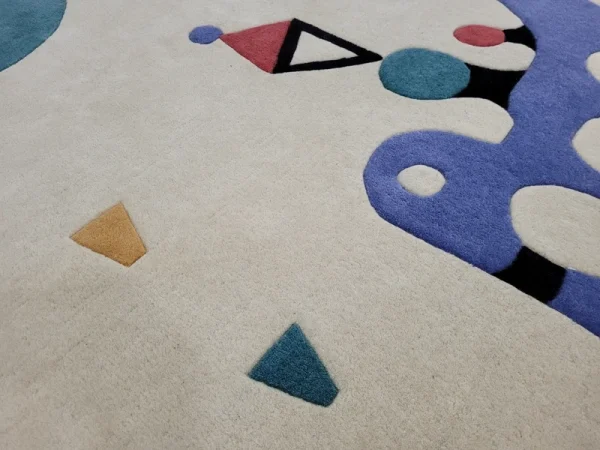 Gros plan sur tapis fait main par Rug Your Life, inspiré du tableau « Composition » (1944) de Wassily Kandinsky. Les couleurs du tapis sont le blanc crème, le bleu, le rouge et le vert.