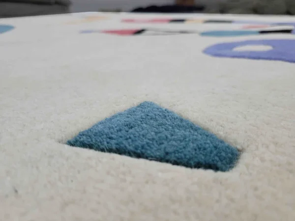 Gros plan sur tapis fait main par Rug Your Life, inspiré du tableau « Composition » (1944) de Wassily Kandinsky. Les couleurs du tapis sont le blanc crème, le bleu, le rouge et le vert.