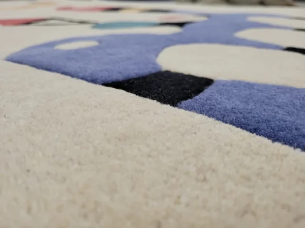 Gros plan sur tapis fait main par Rug Your Life, inspiré du tableau « Composition » (1944) de Wassily Kandinsky. Les couleurs du tapis sont le blanc crème, le bleu, le rouge et le vert.
