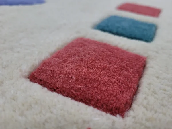 Gros plan sur tapis fait main par Rug Your Life, inspiré du tableau « Composition » (1944) de Wassily Kandinsky. Les couleurs du tapis sont le blanc crème, le bleu, le rouge et le vert.